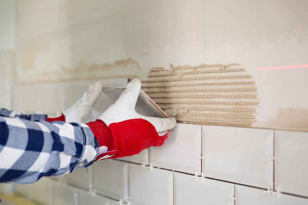 A person wearing gloves is laying tile for a backsplash in a kitchen.