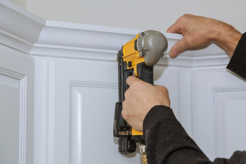 A picture of a person using a nail gun to install cabinet trim.