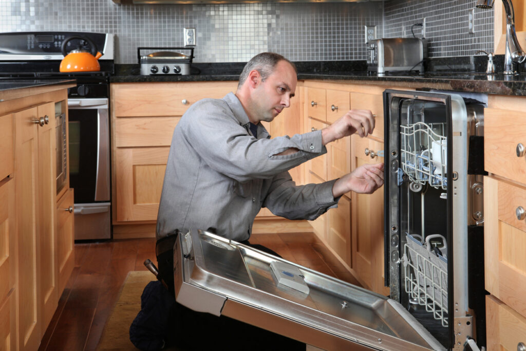 A person, inspecting an opened dishwasher in a kitchen.
