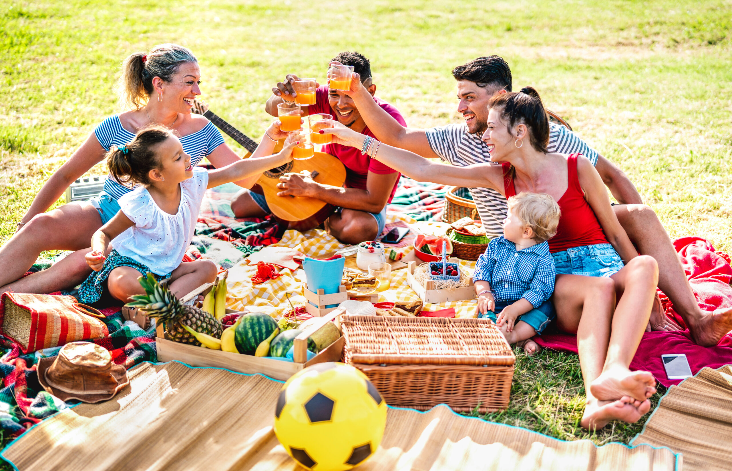 Families having fun together with kids at pic nic barbecue party - Joy and love life style concept with mixed race people toasting juices with children at park