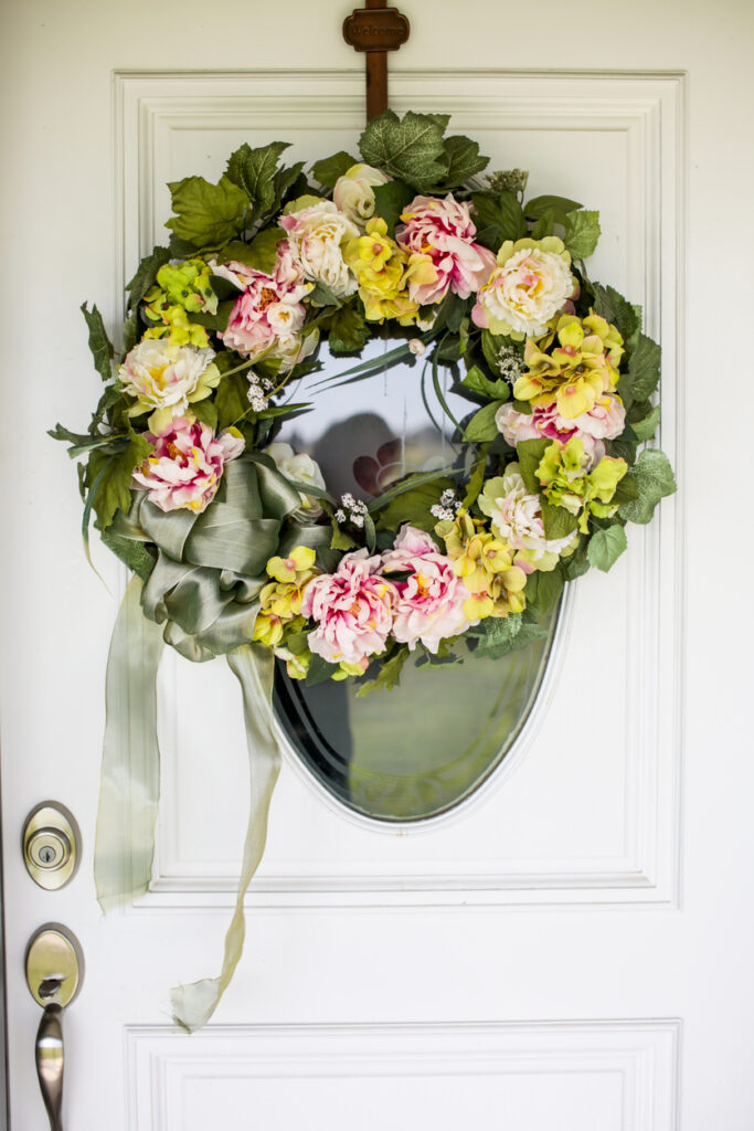 A close-up of a white door with a floral wreath on it, showing the delicate details of the flowers.