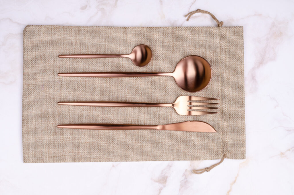 A set of golden utensils on a rose gold placemat.