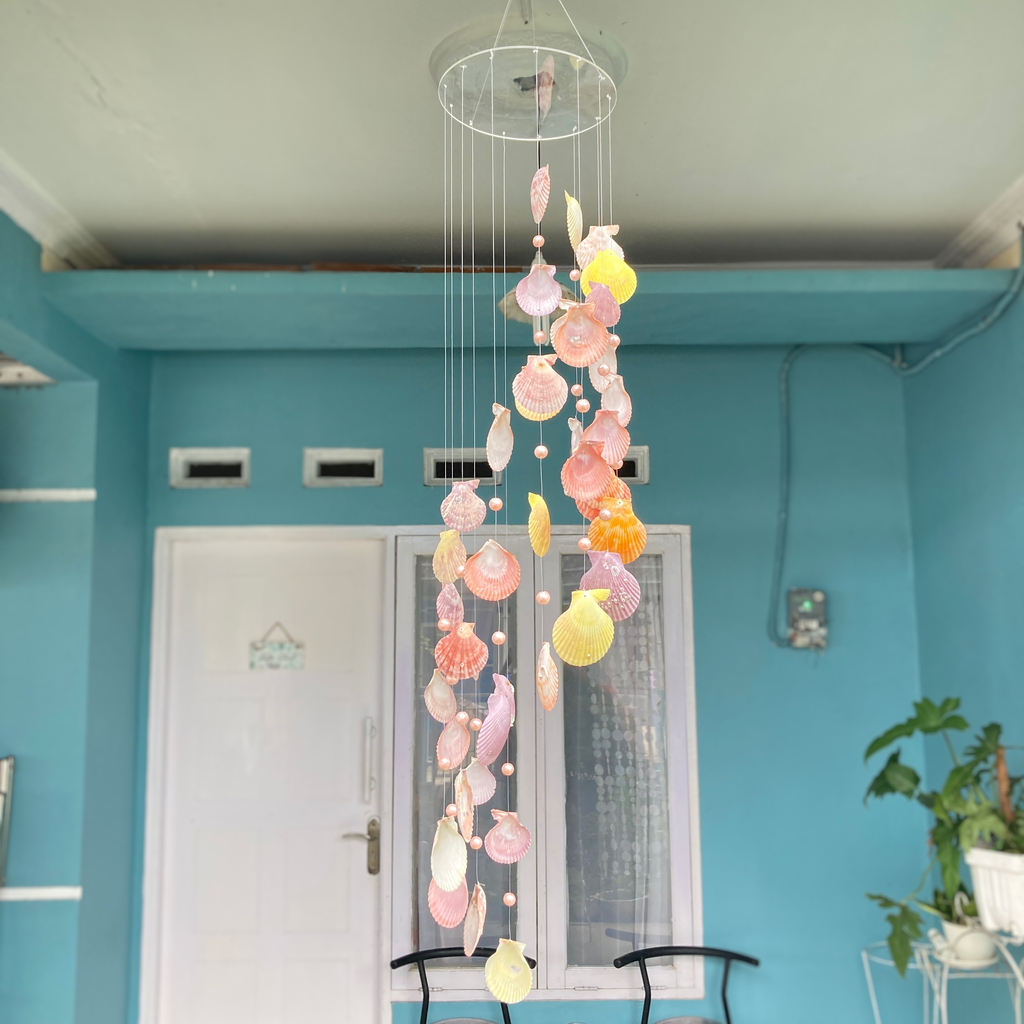 A colorful seashell wind chime hanging from a white ceiling, with strings of shells in various shapes and sizes.